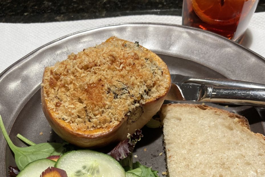 A photo of a stuffed butternut squash bottom with salad, bread and a cocktail