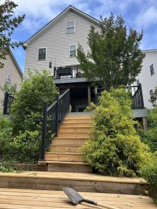 Wooden stairway descends from house and patio through garden areas on a slope.