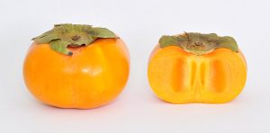 A full and halved persimmon against a white background